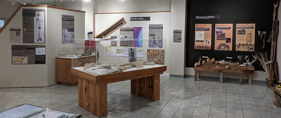 an elegant dress and hand fan sit in a display case surrounded by colorful exhibits and imagery of the island's history