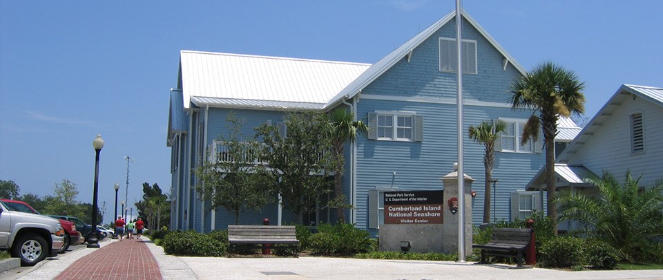 Two story blue building along brick walkways, with American flag flying