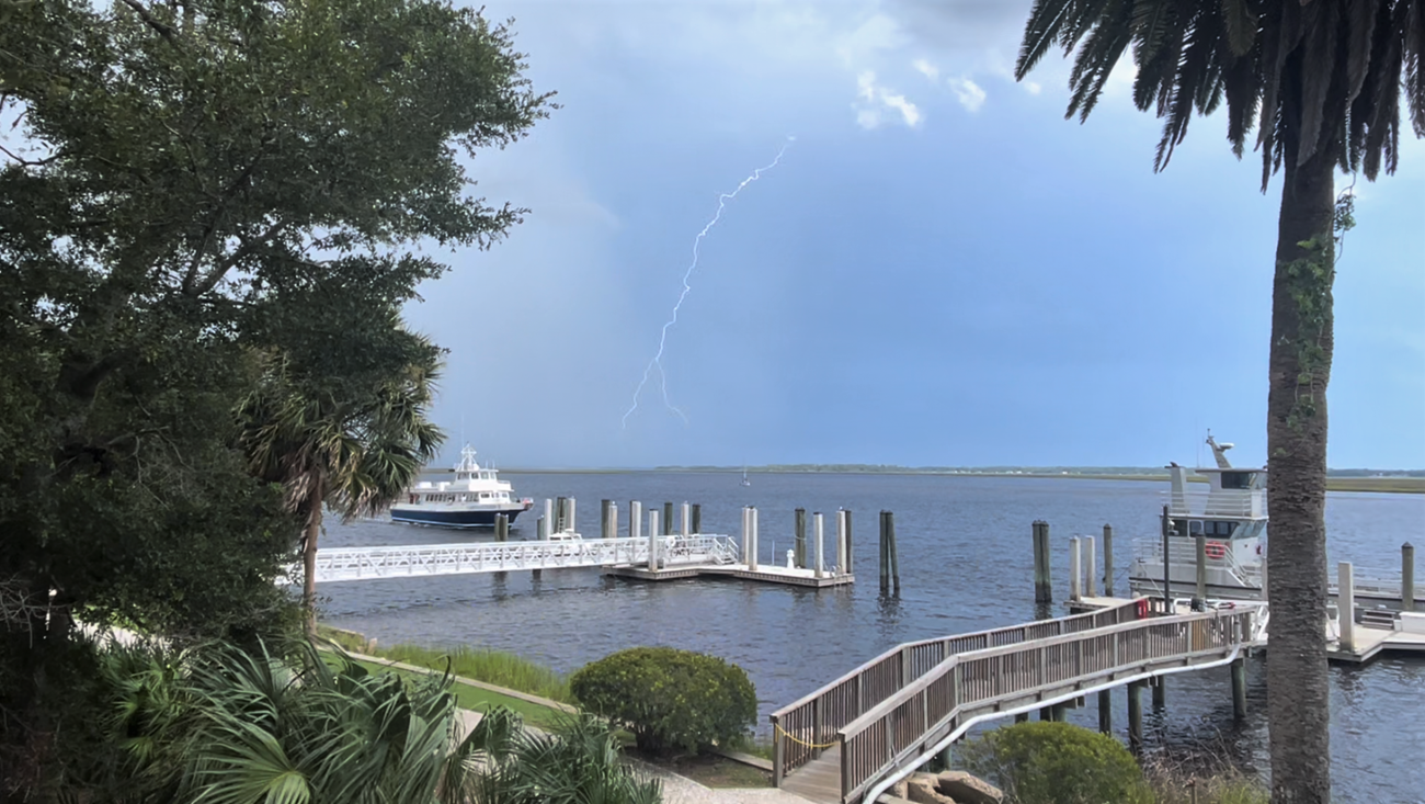 Ferry approaching a dock with dark skies and a lightning strike in the background