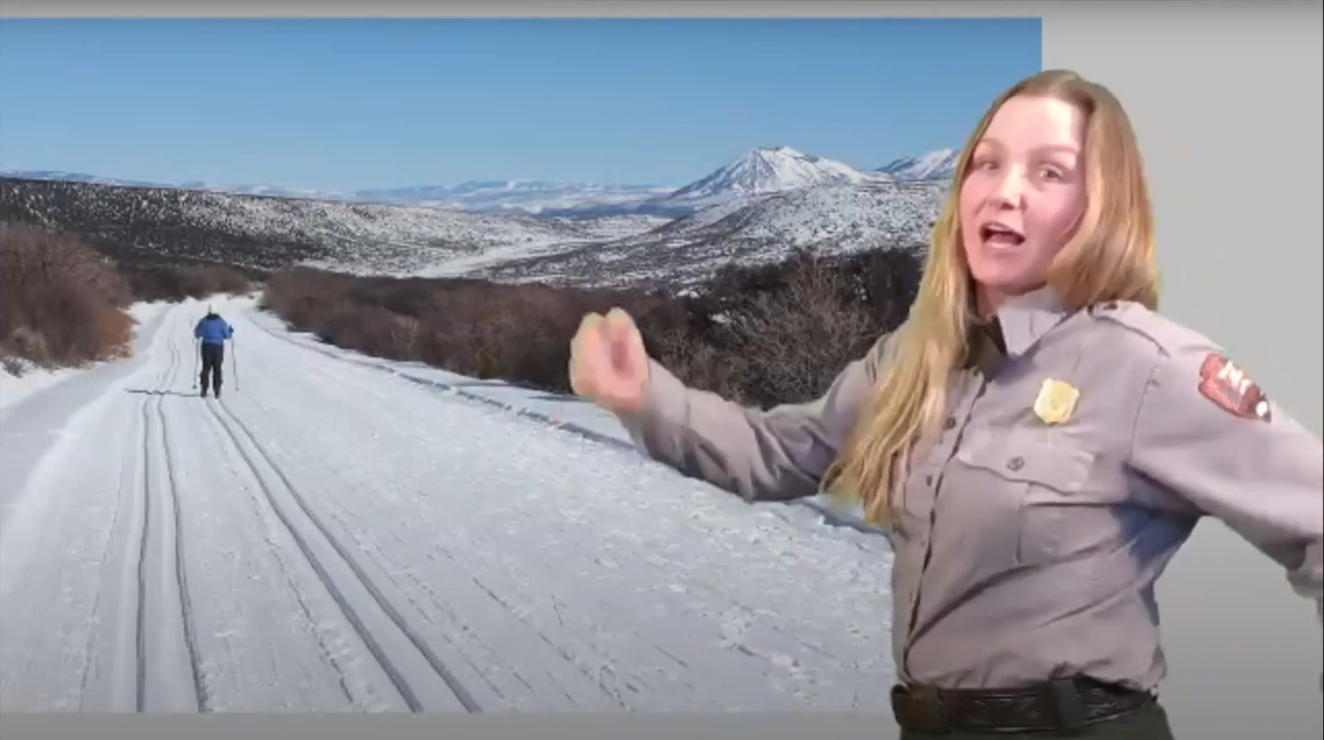 Park ranger stands in front of a screen with winter scene. They are demonstrating how to snowshoe.