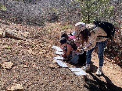 A group of students complete worksheets on clipboards alongside a dirt trail.