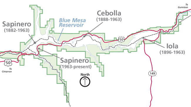 Map showing a reservoir in blue and land in green. A black railroad line crosses the map. Three towns are labeled with a grey dot and line.