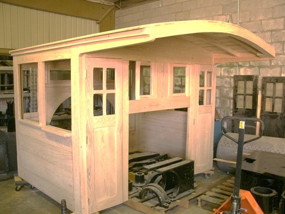 A wooden railcar cab with windows and an overhanging roof. Tools are visible around it.