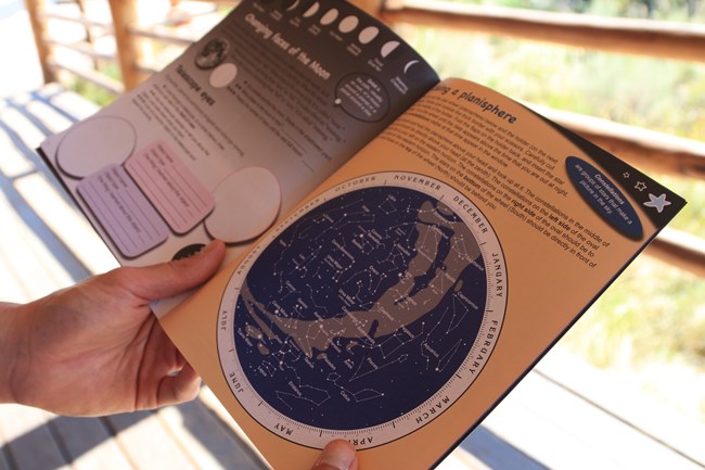 A person holds an activity booklet open with pages showing astronomy information