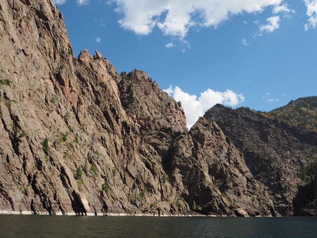 Layered rocks of a canyon wall rising high above a blue body of water