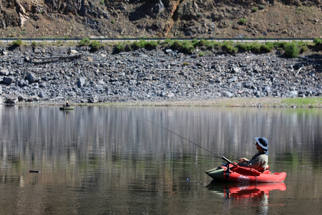 A person fishing out of a small red inflatable boat