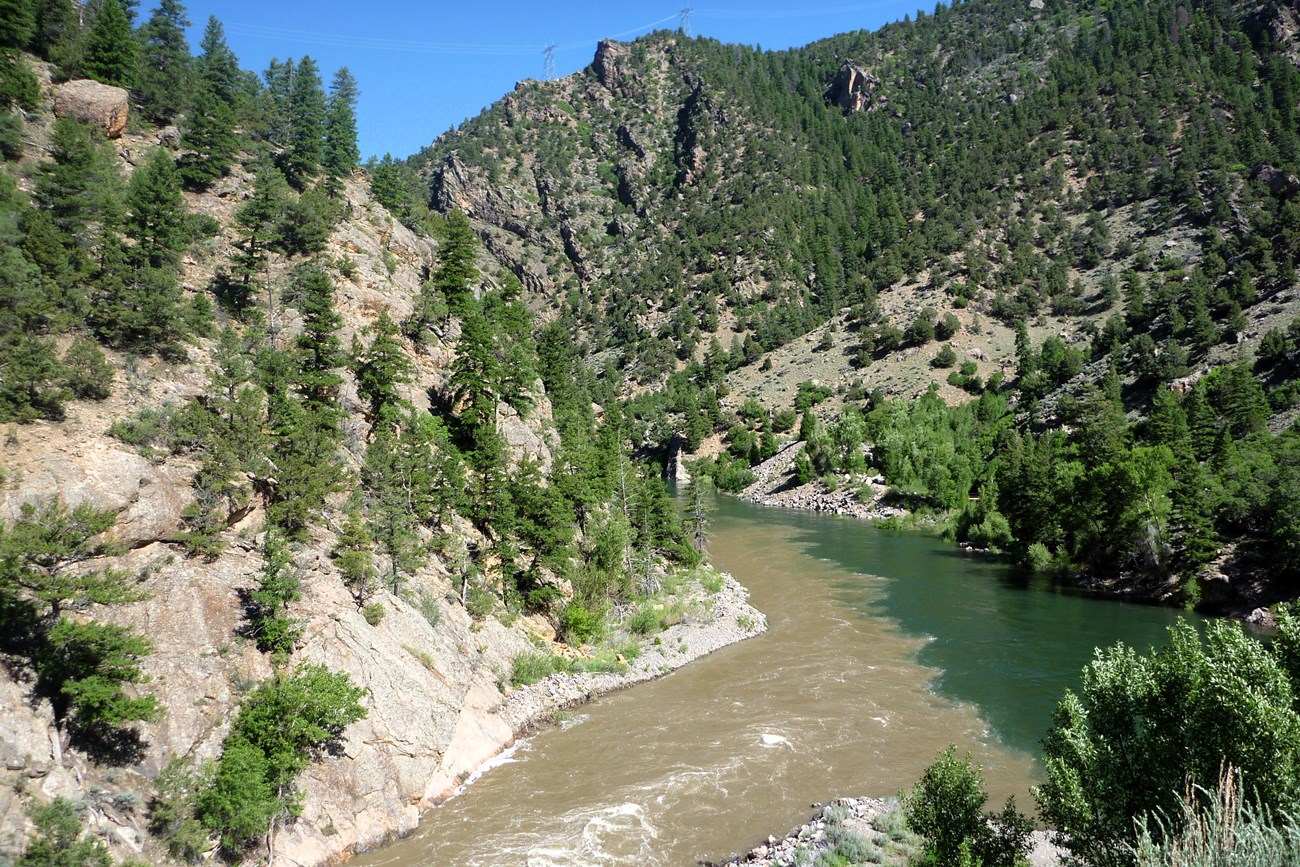 The confluence of a silty river into a clear larger one between canyon walls