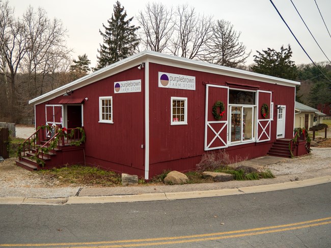 A red building with white trim and barn-style doors with signs on two sides that read, "purplebrown Farm Store."