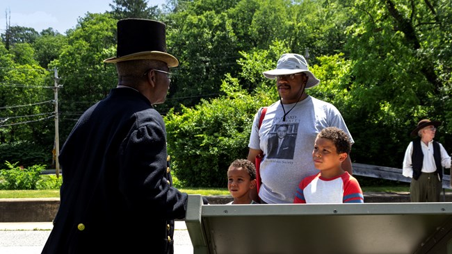 A father and his two sons listen to a man in a top hat talk.