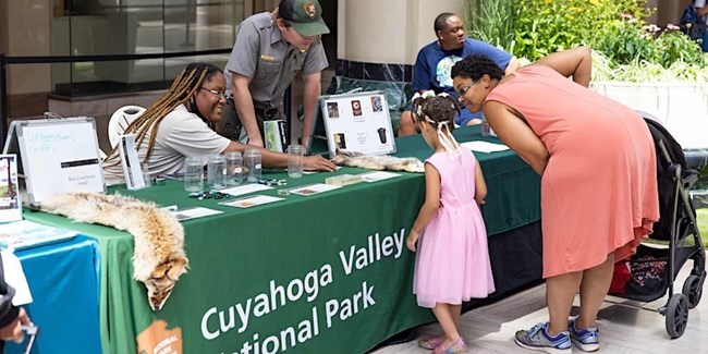 A ranger and a volunteer talk to a family at a table.