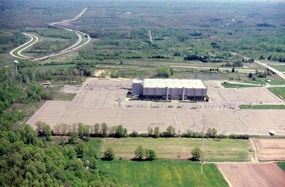 aerial view of a large white rectangular building surrounded by gray parking lots larger than the building itself.