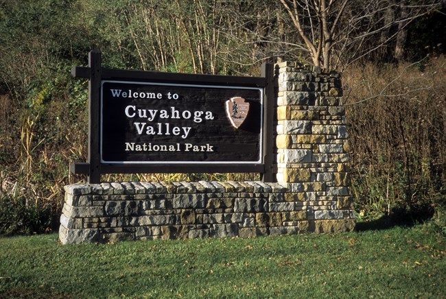 A brown wooden sign on stone base with white text: Welcome to Cuyahoga Valley National Park.