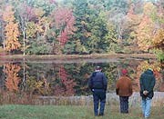 Three Visitors take a moment to enjoy the reflection of fall trees in the glassy waters of Sylvan Pond.
