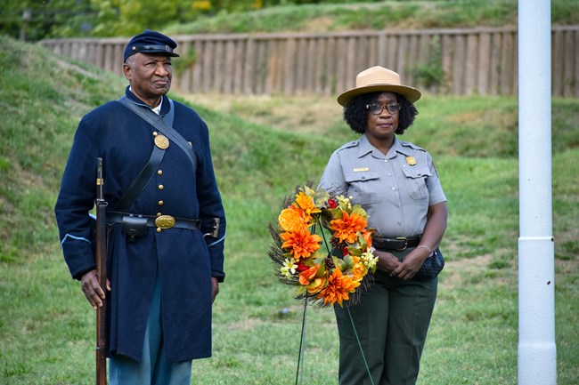 a park ranger and a historical reenactor stand behind a wreath
