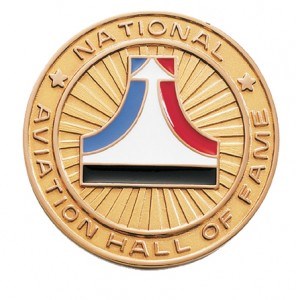 Aviation Hall of Fame logo on a gold seal with a red and blue line curving up to the top with an arrow representing a plane on top