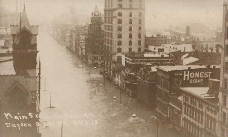 An old photo showing very high water on a street between several buildings in a downtown area of Dayton, Ohio.