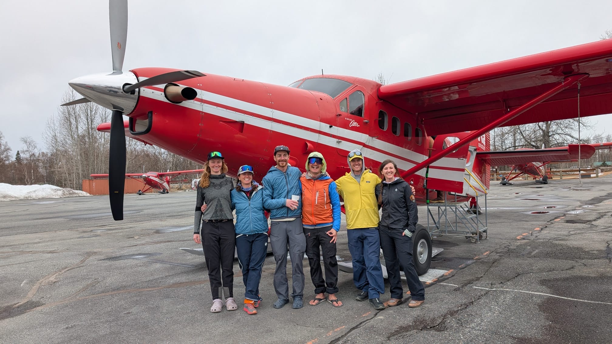 6 rangers and volunteers smiling and standing in a line, arm-in-arm, in front of a red plane
