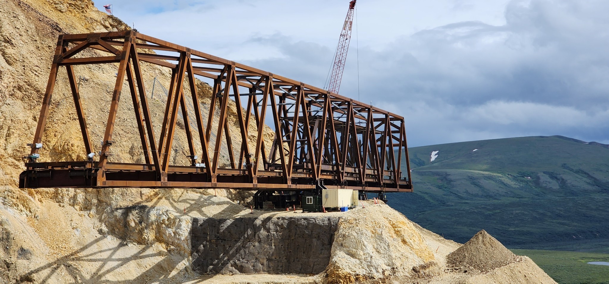 View from the west side of the main bridge truss and half of the launch truss erected inside. Behind the bridge is a tall crane.