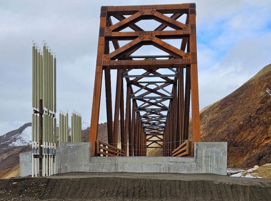 Photo taken from the east end looking straight through the center of the bridge. In the center at the entrance to the bridge are large concrete blocks, and on the left are several tall cylindrical structures.