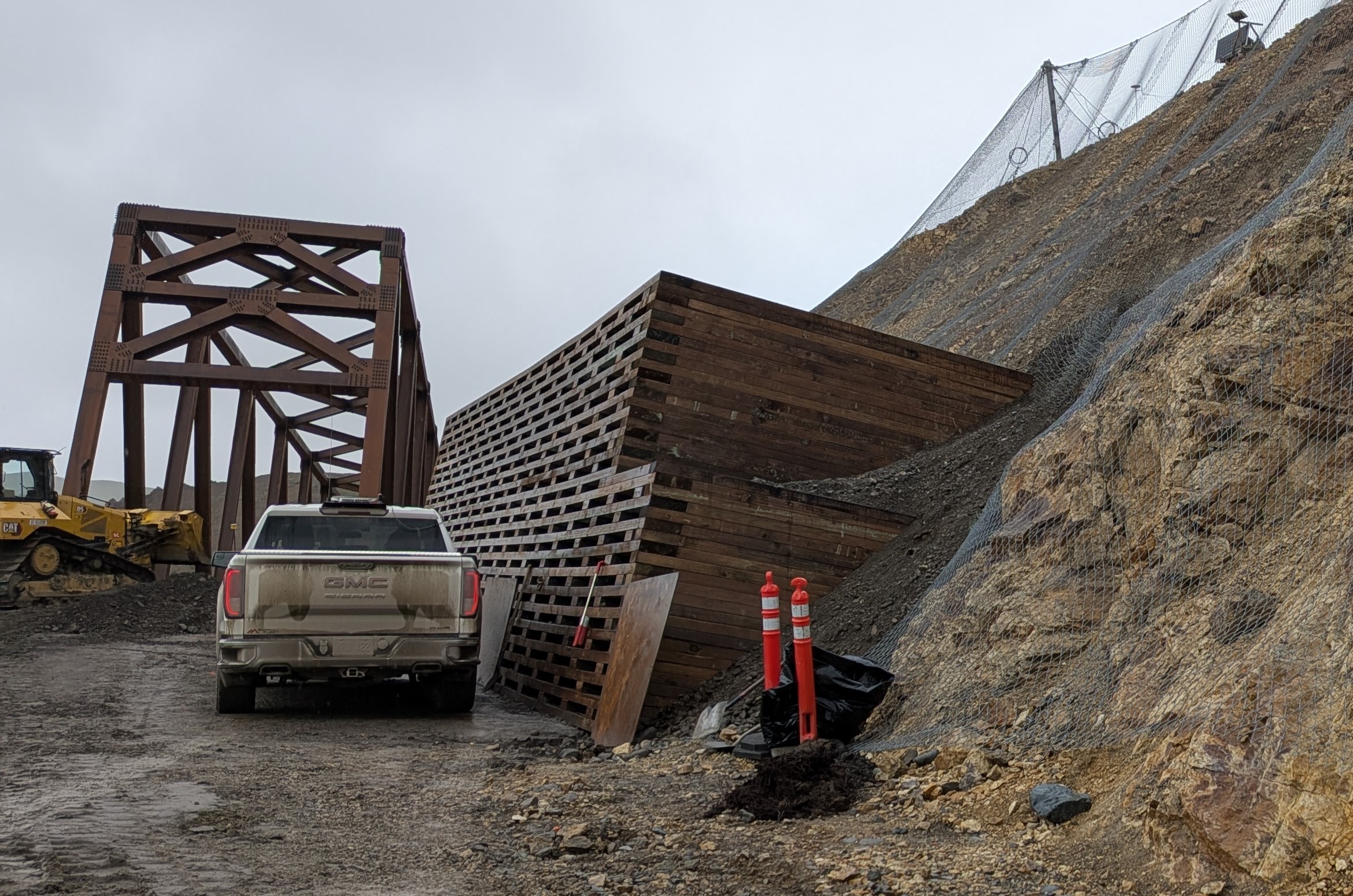 A large wooden wall built into a steep rock slope, next to the east end of the bridge.