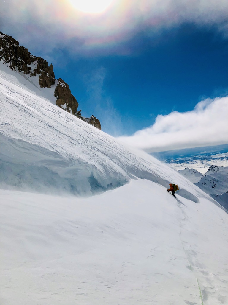 A climber ascends a snow slope in a light blowing mist