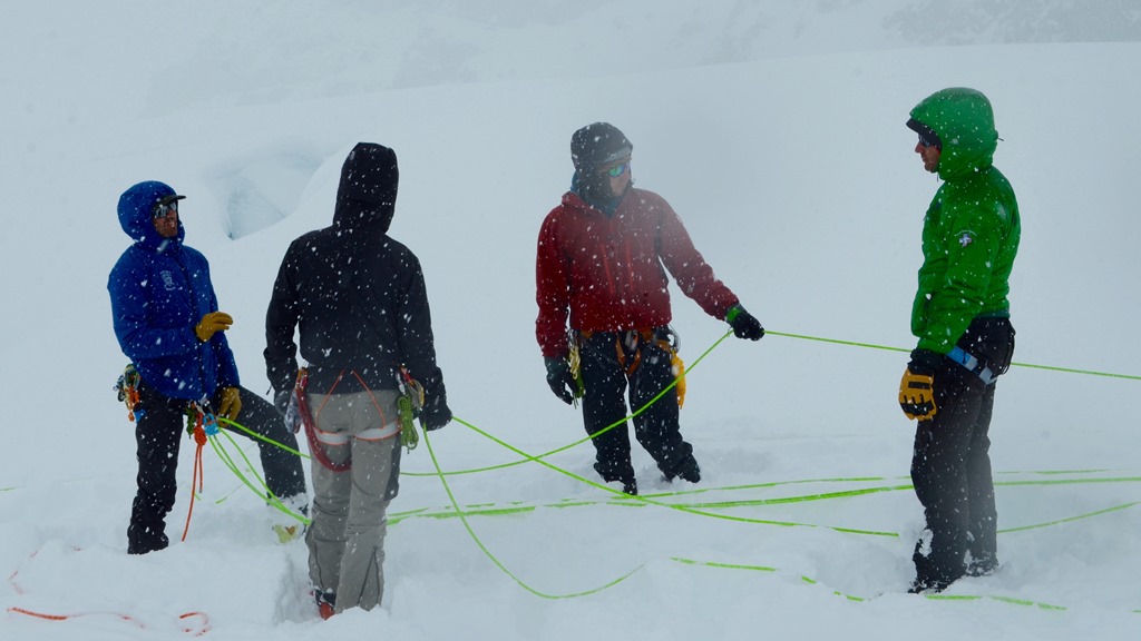 Four roped mountaineers discuss crevasse rescue skills in snowy conditions