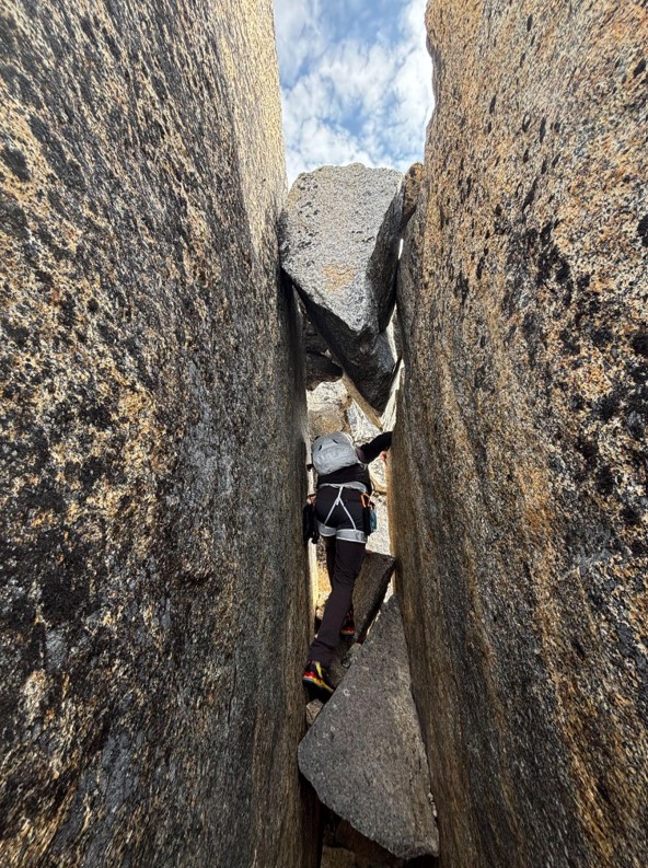 A ranger climbs through a rocky crevasse