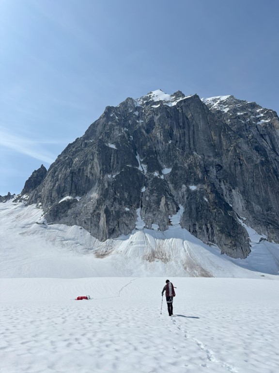 Ranger walks across a snowy field toward a red tent with mountain peaks in the background