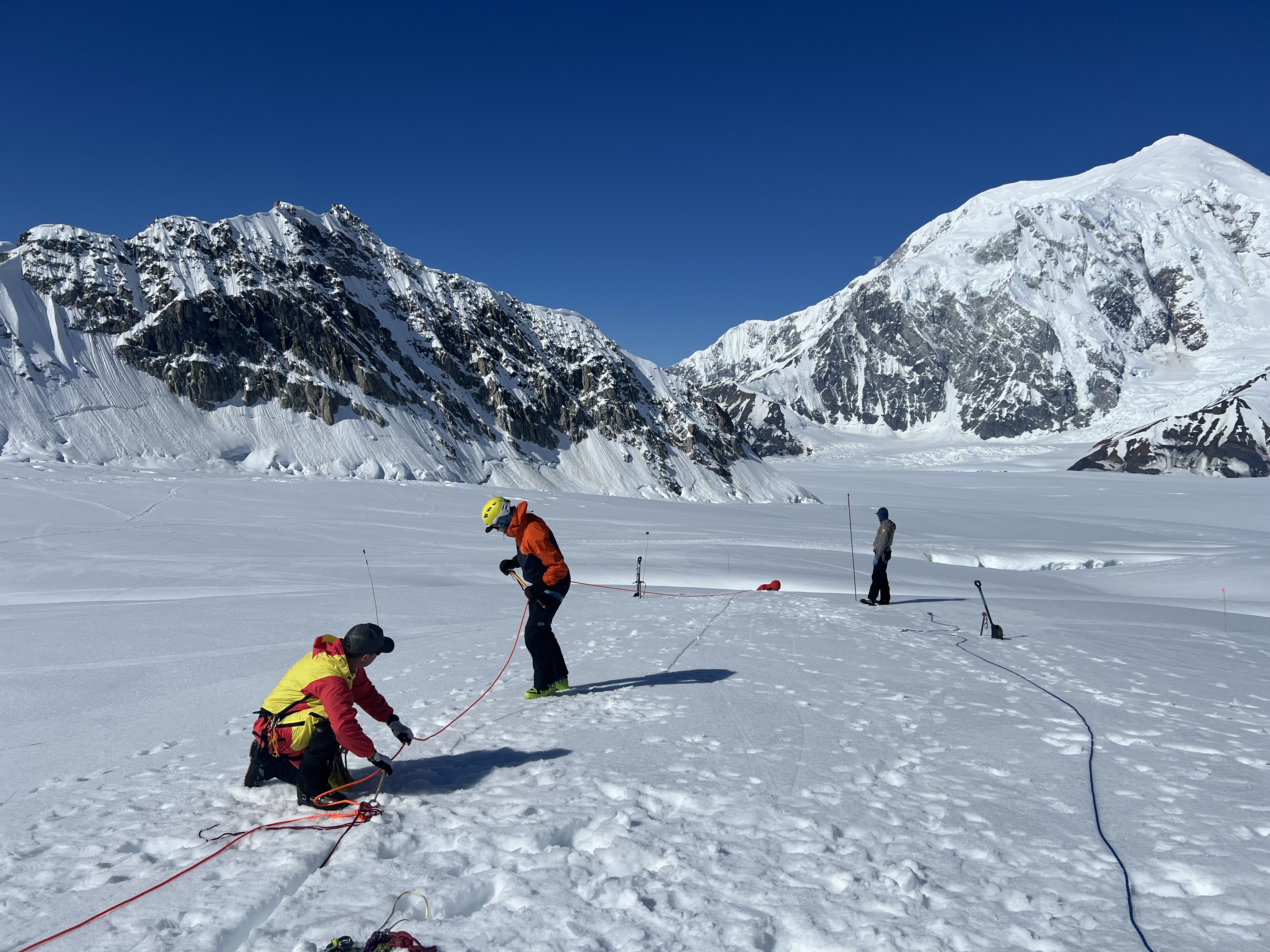Climbers set up a pulley system on the glacier surface, with the head of a fourth climb starting to disappear into a crevasse