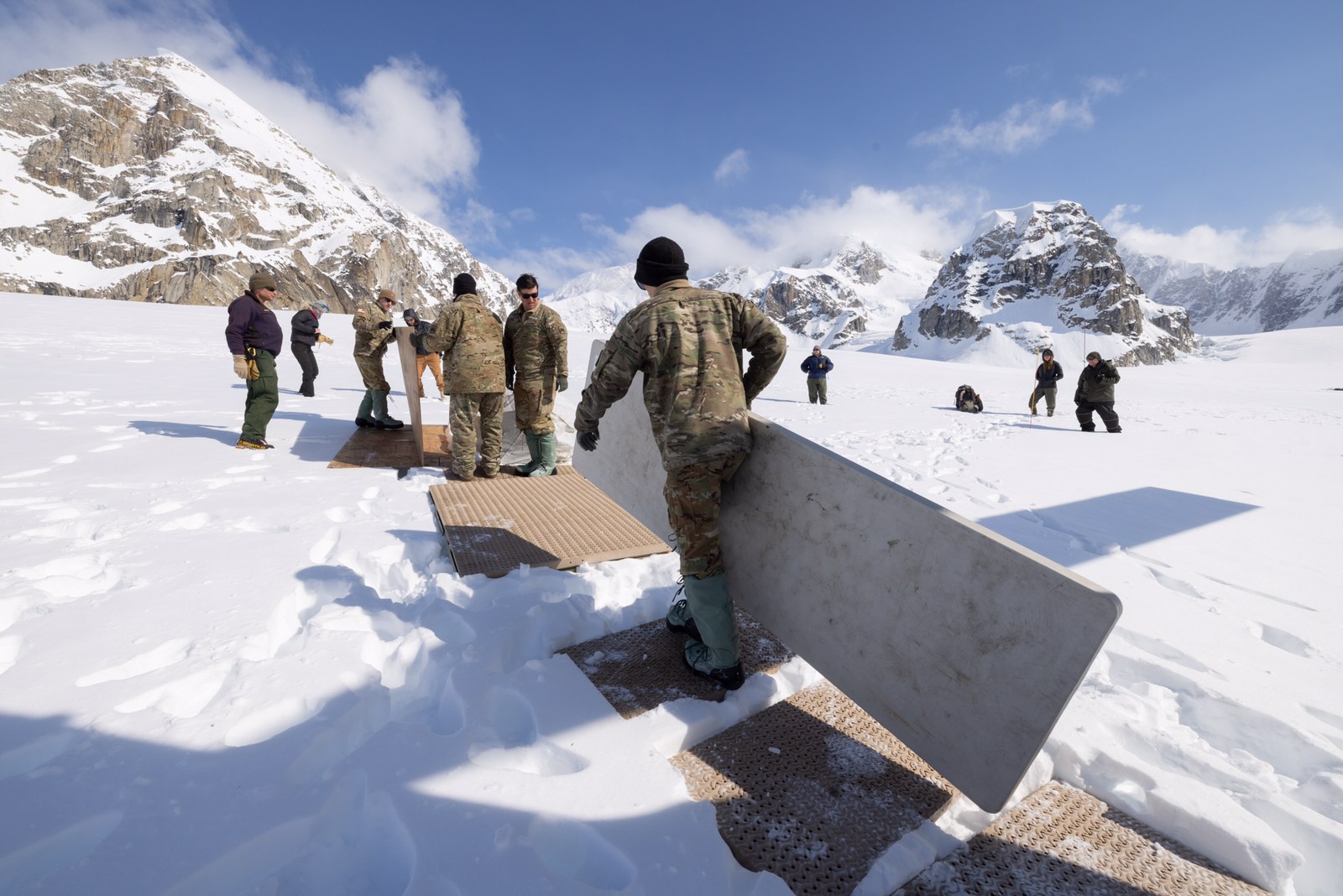 Soldiers in camoflage haul camp gear on a snowy glacier