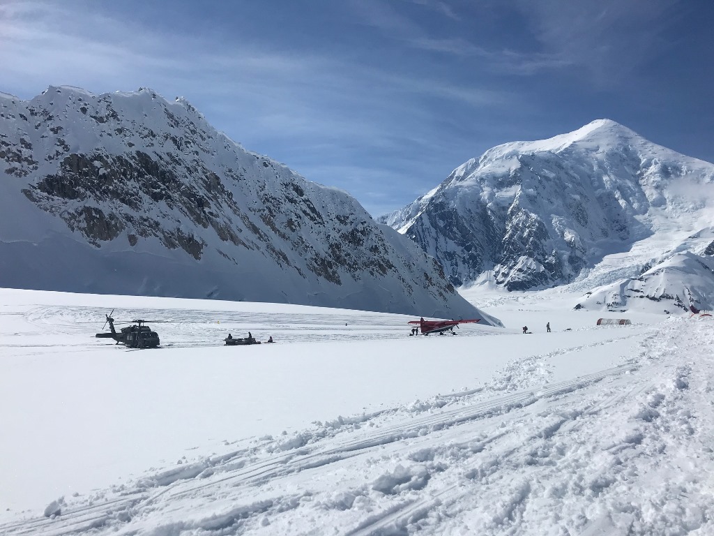 A glacier landing strip with a helicopter, an airplane, and tents