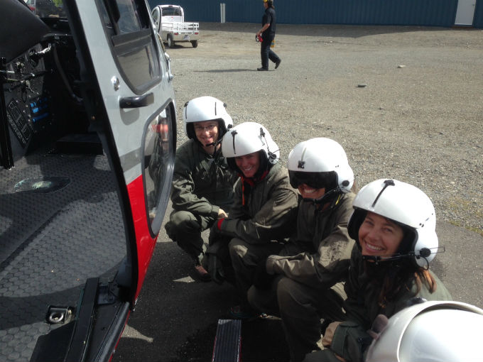 Four volunteers in flight helmets crouched next to helicopter