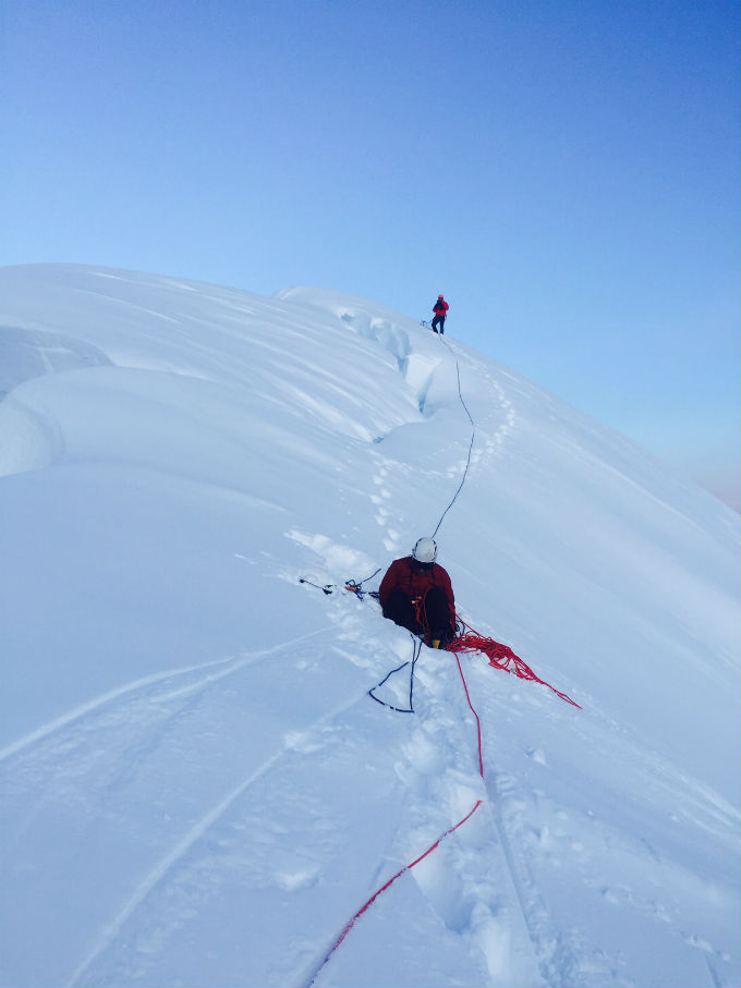 Two roped climbers approach the snowy summit of Mount Huntington