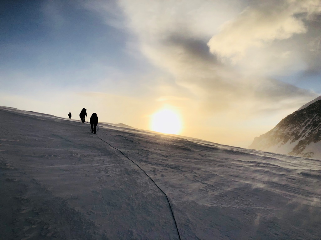 A rope team climbs a snowy ridge during sunset