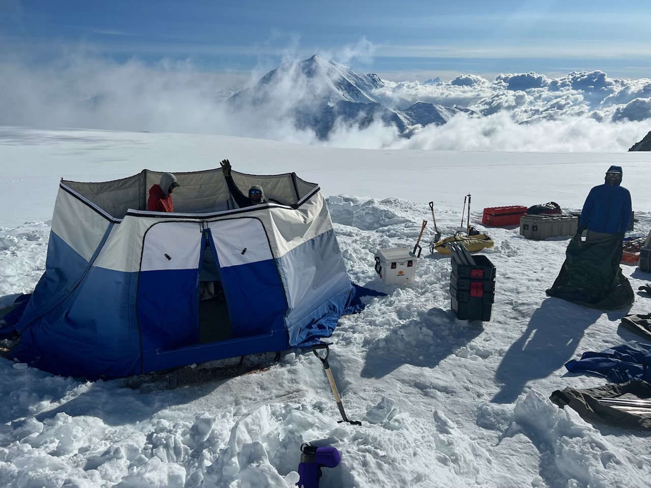 A ranger patrol disassembles a blue tent on a glacier