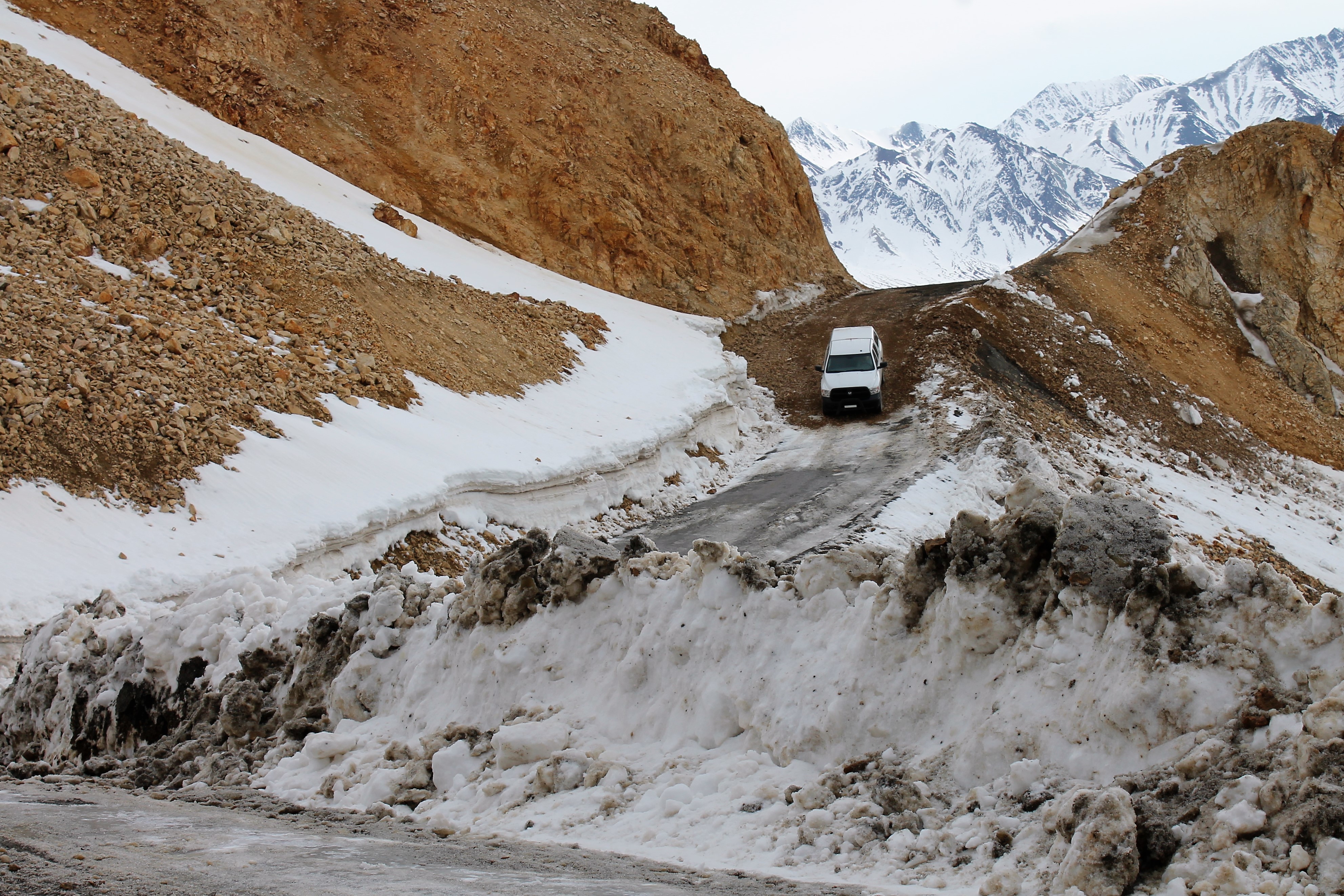 a truck driving downhill on a steep dirt road atop a mountain covered in snow