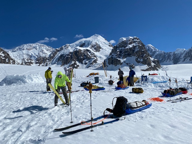 A team readies their packs, skis, and sleds