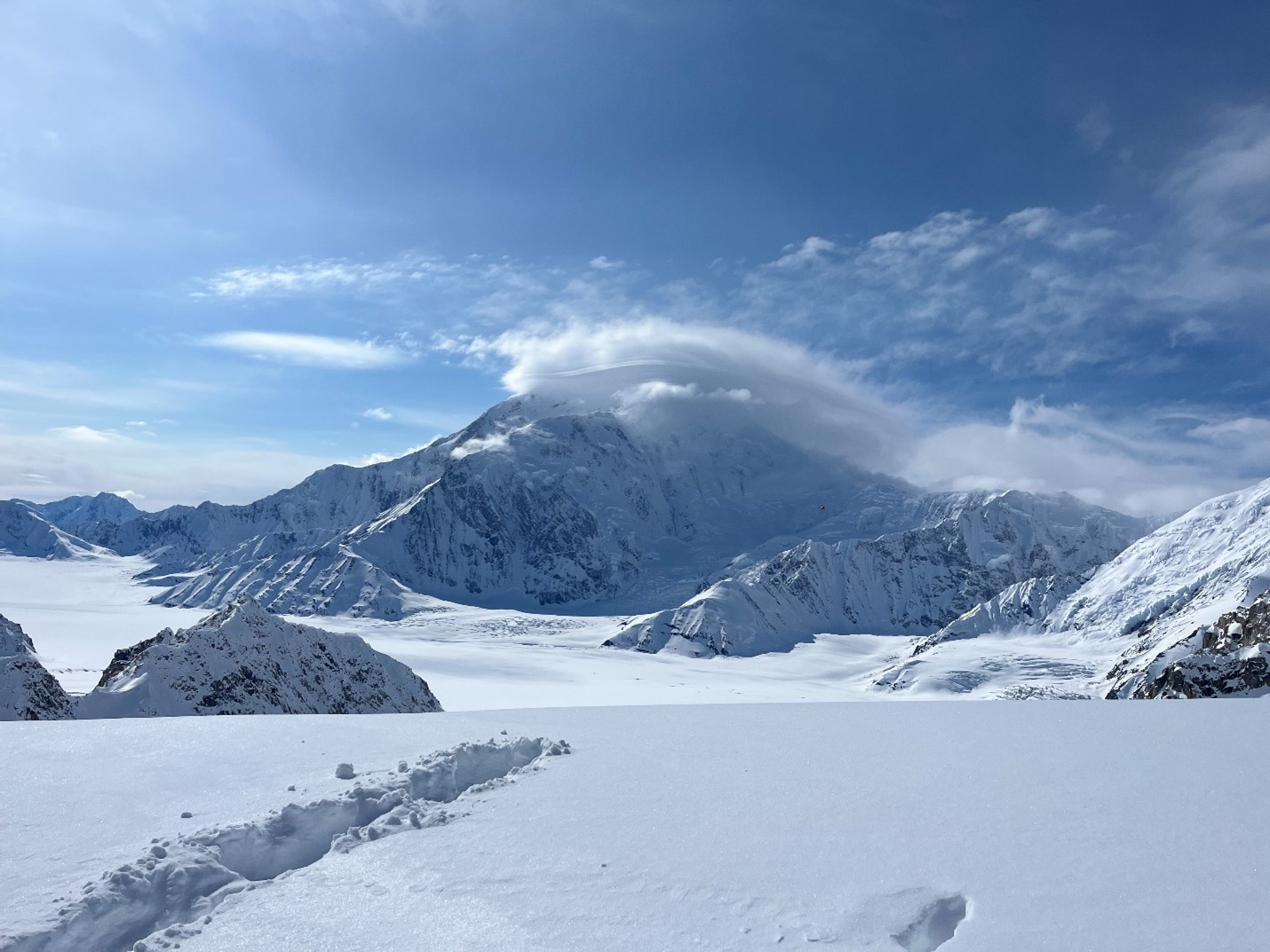 View of a snowy mountain against a bright blue sky with wispy clouds over the peak 