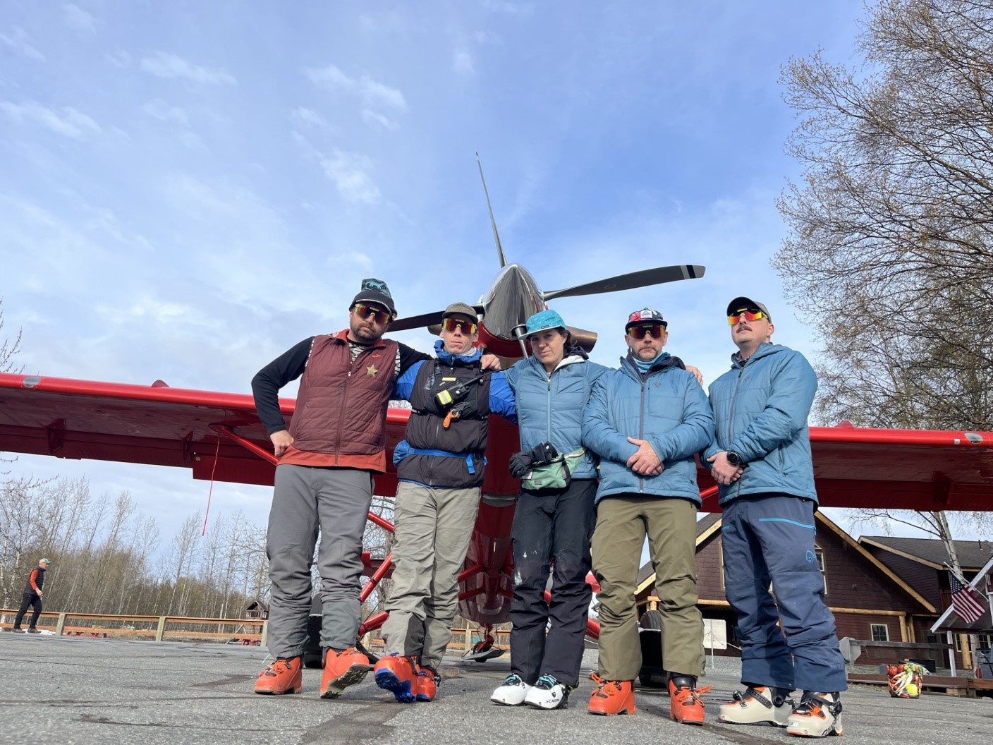 Five mountaineering rangers pose in front of a red plane