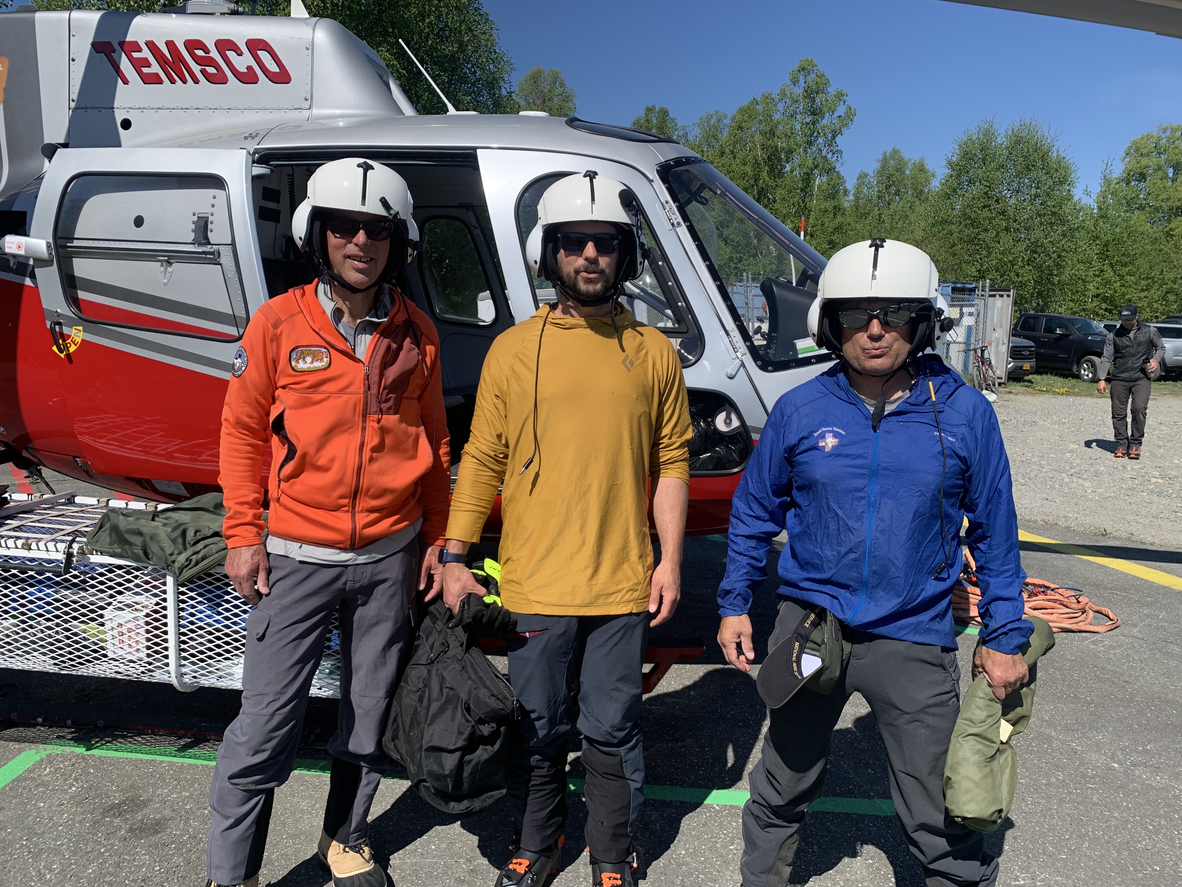 Three climbers stand outside the open door of a helicopter