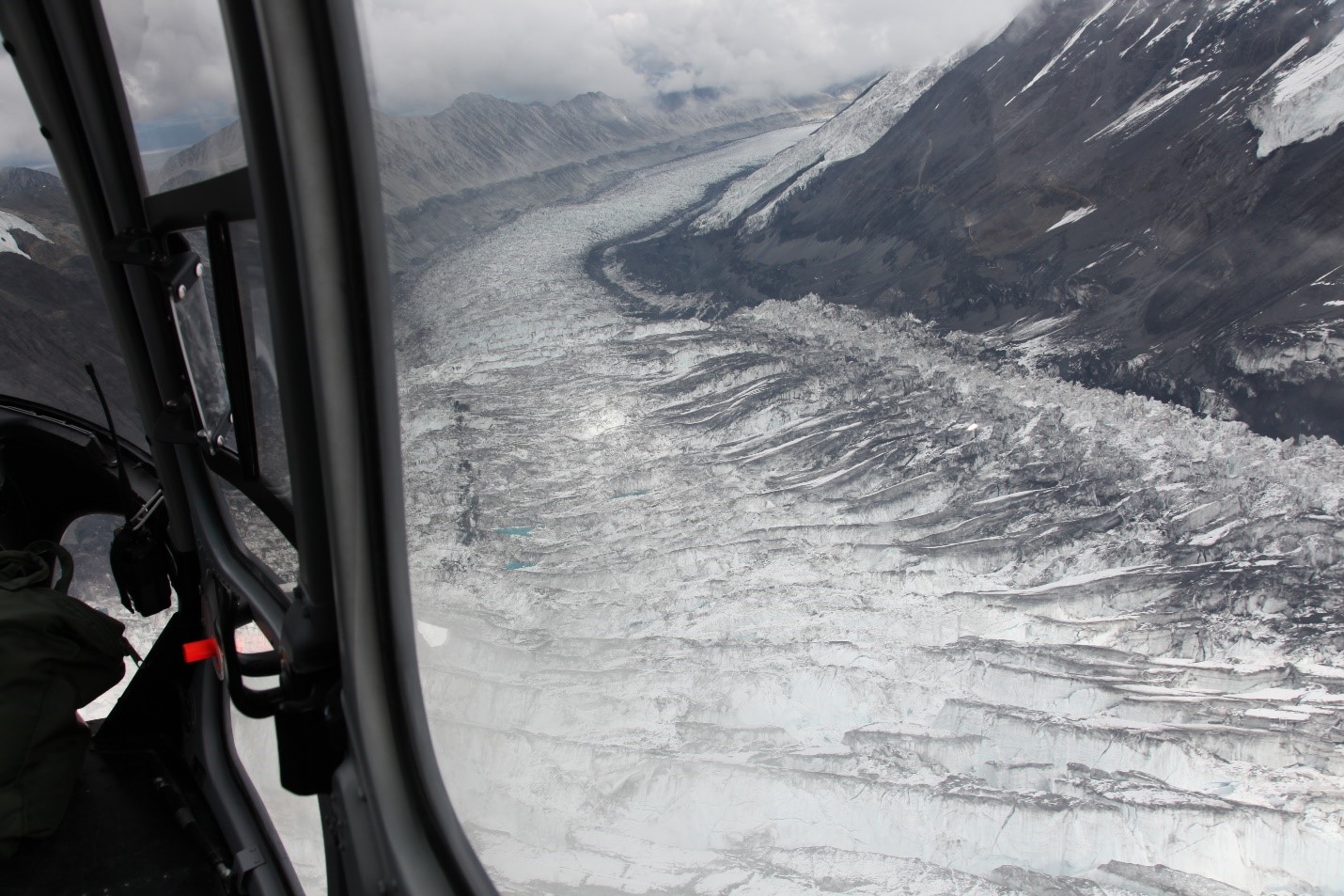 View out a helicopter window of heavily crevassed glacier surface