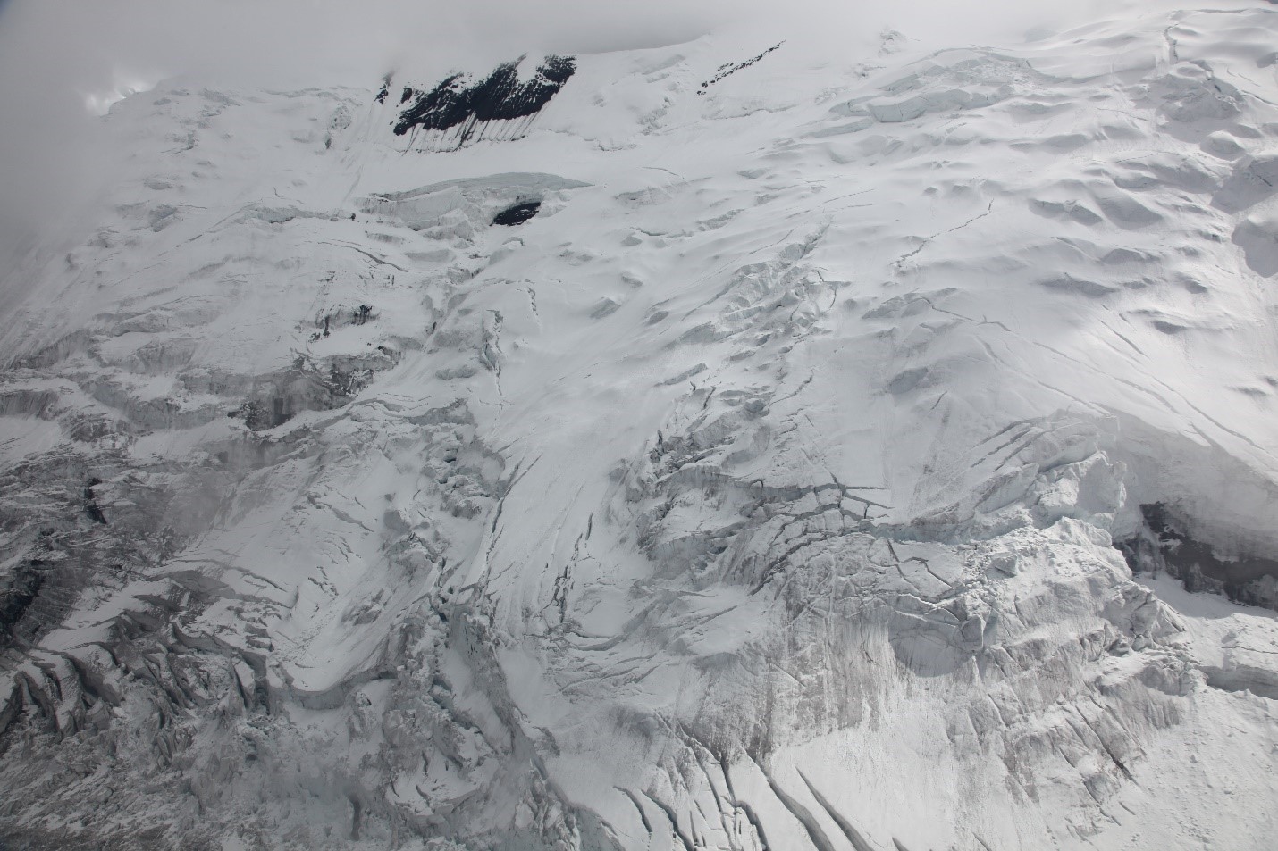 View of crevassed and snowy surface rising steeply upward from the lower glacier surface