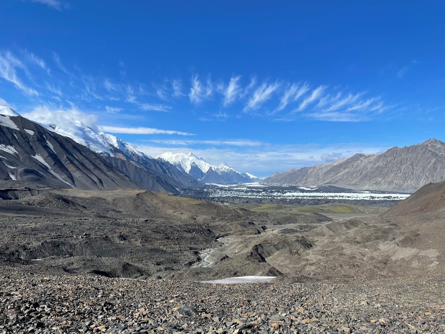 View of a rocky glacial moraine with bright blue sky and snow covered peaks in the distance