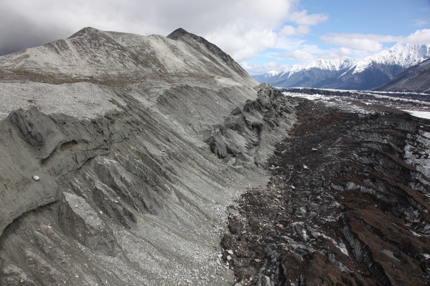 Image of glacial moraine.  Pale-colored fine gravel covers a steep slope down to a jumbled glacier covered in darker rocks