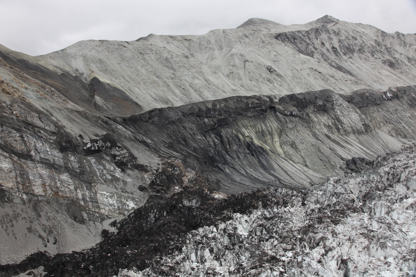 View of a multi-tiered rocky interface between glacier ice and a mountainside.