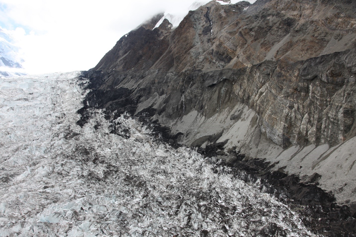 View of multi-textured interface between jumbled glacier ice and a steep rock face