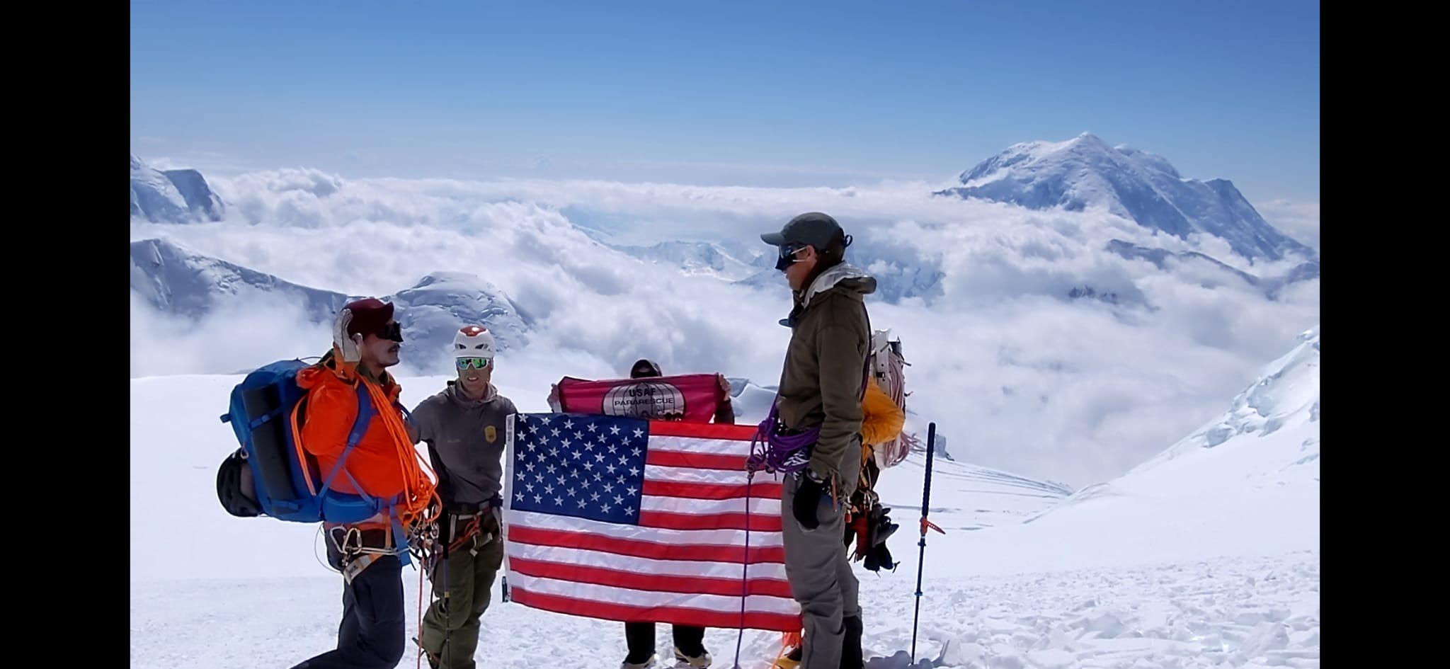 A climber takes an oath in front of an American flag with Mount Hunter in the backdrop