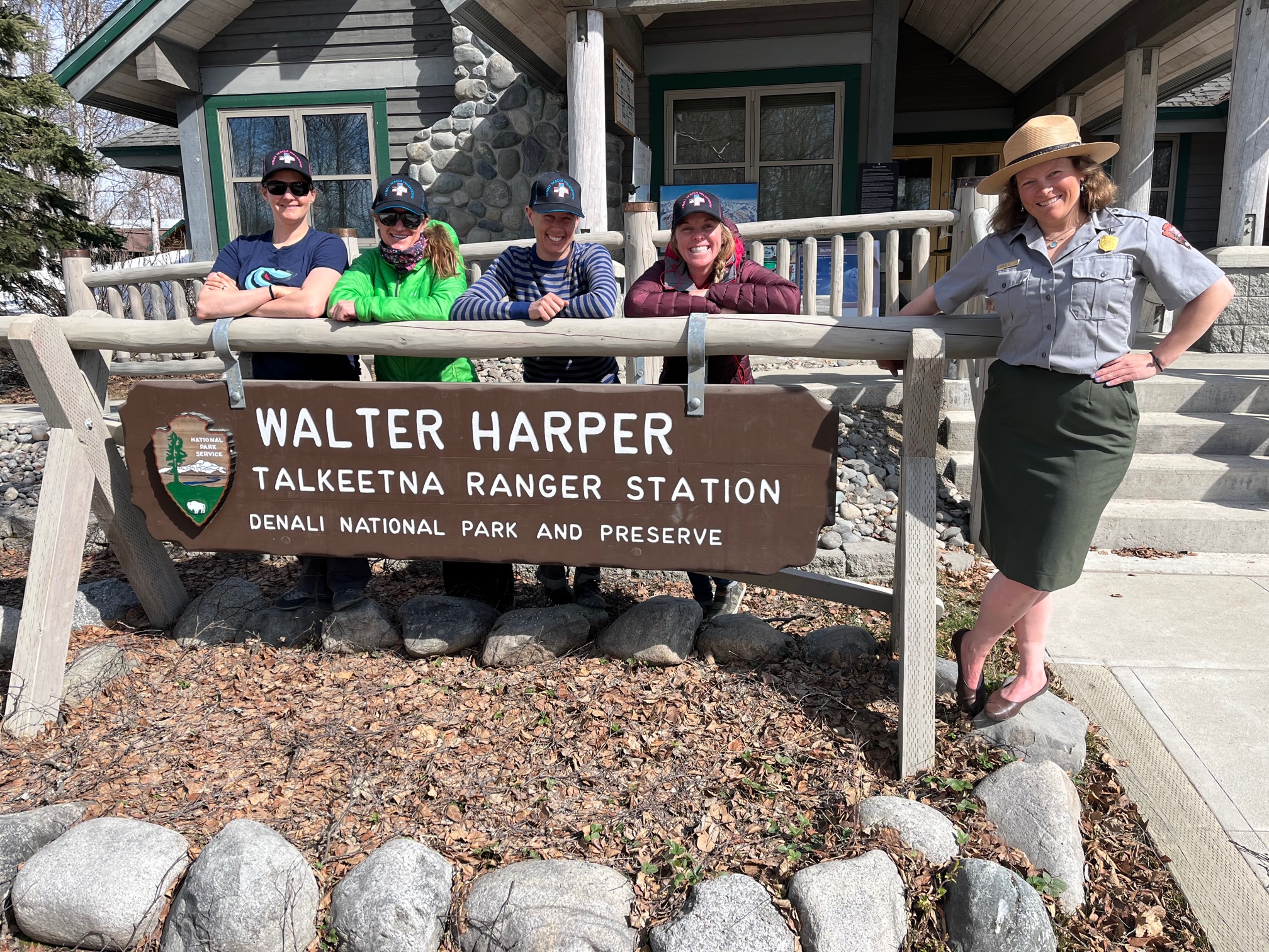 Five women stand around the Walter Harper Talkeetna Ranger Station sign