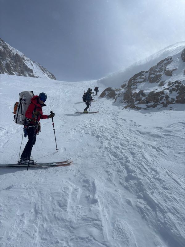 Three rangers on skis in a line going up a snowy ridge