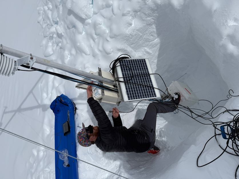 A volunteer dressed in black checks a weather station in the snow